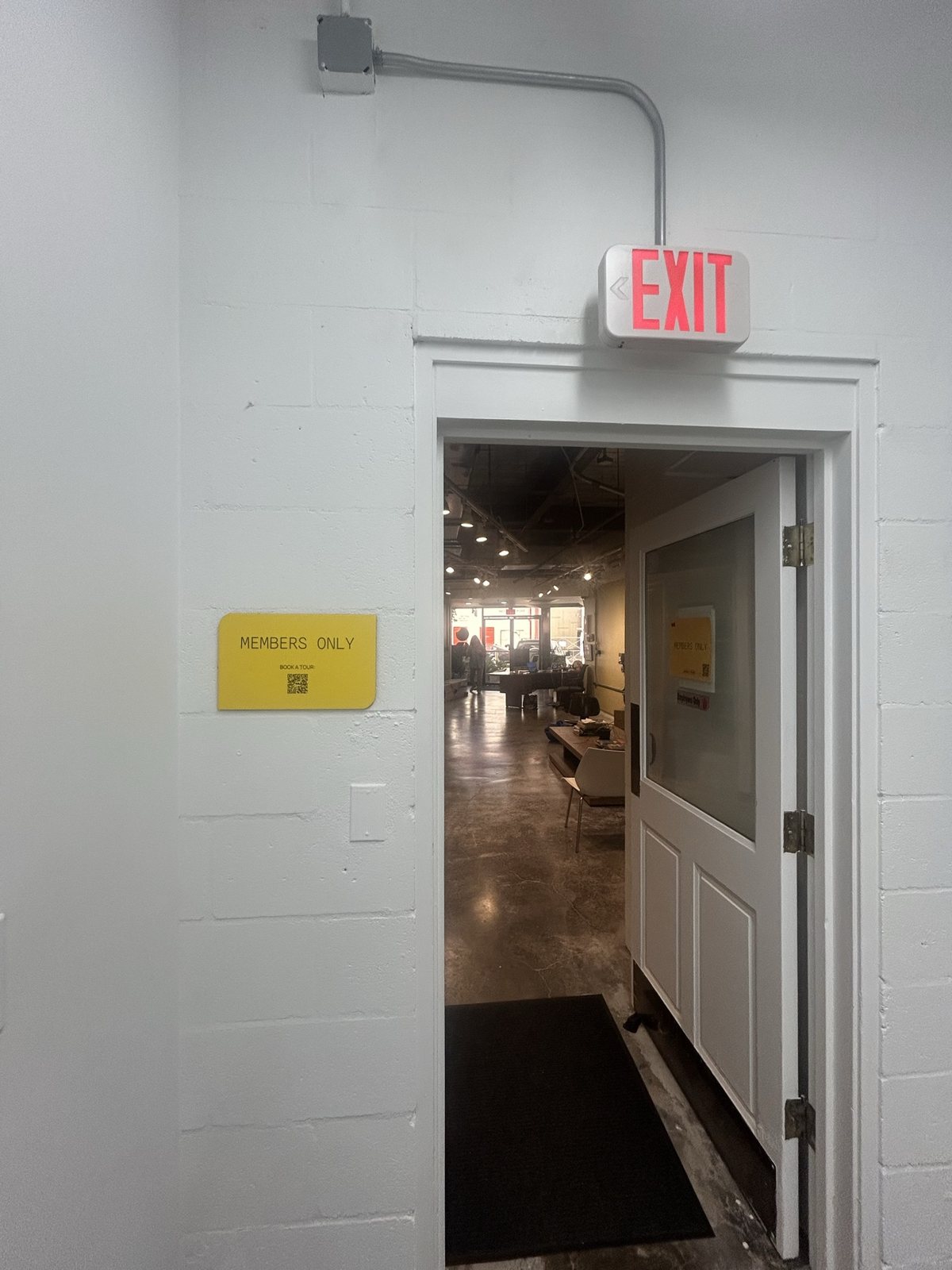 An open door with an exit sign, leading into the workspace