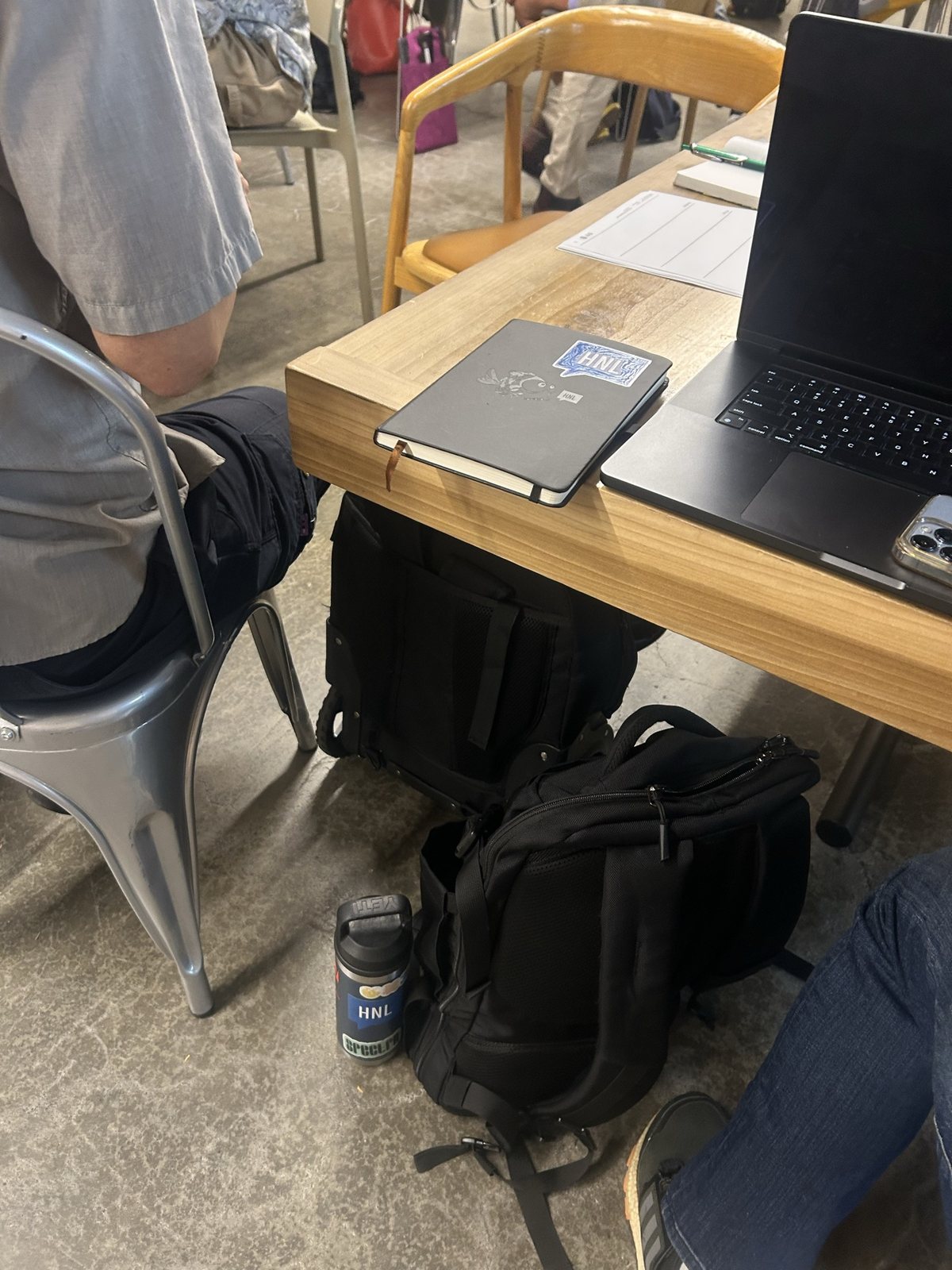 A laptop and notebook at a workshop table, backpacks on the floor
