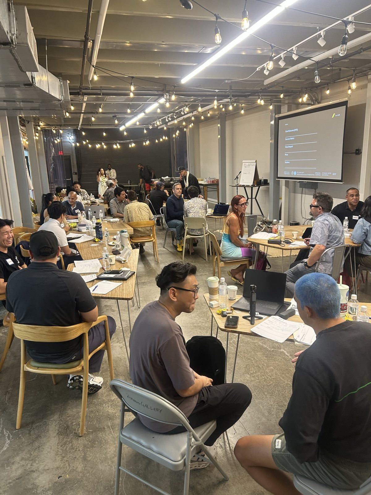 Attendees at tables across the OurSpace floor, screen at the back