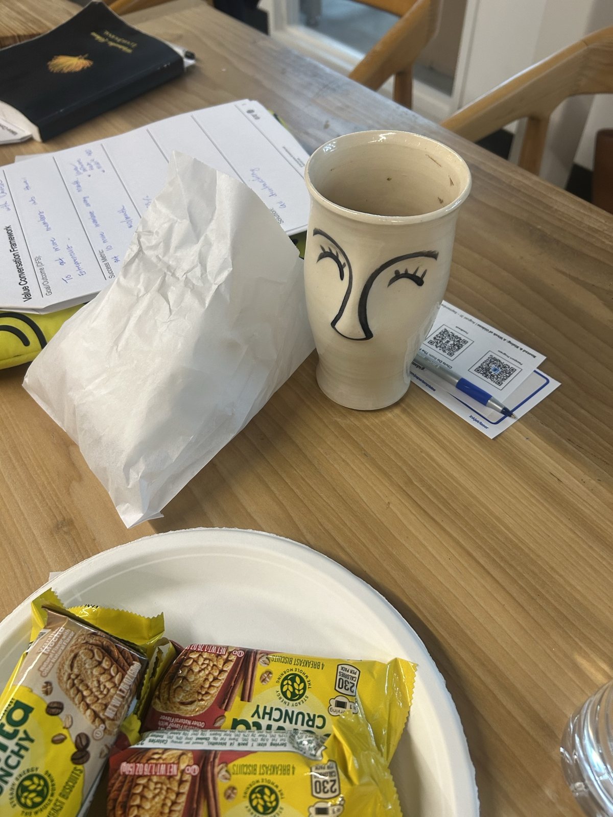 A mug with a face drawn on it, beside breakfast biscuits