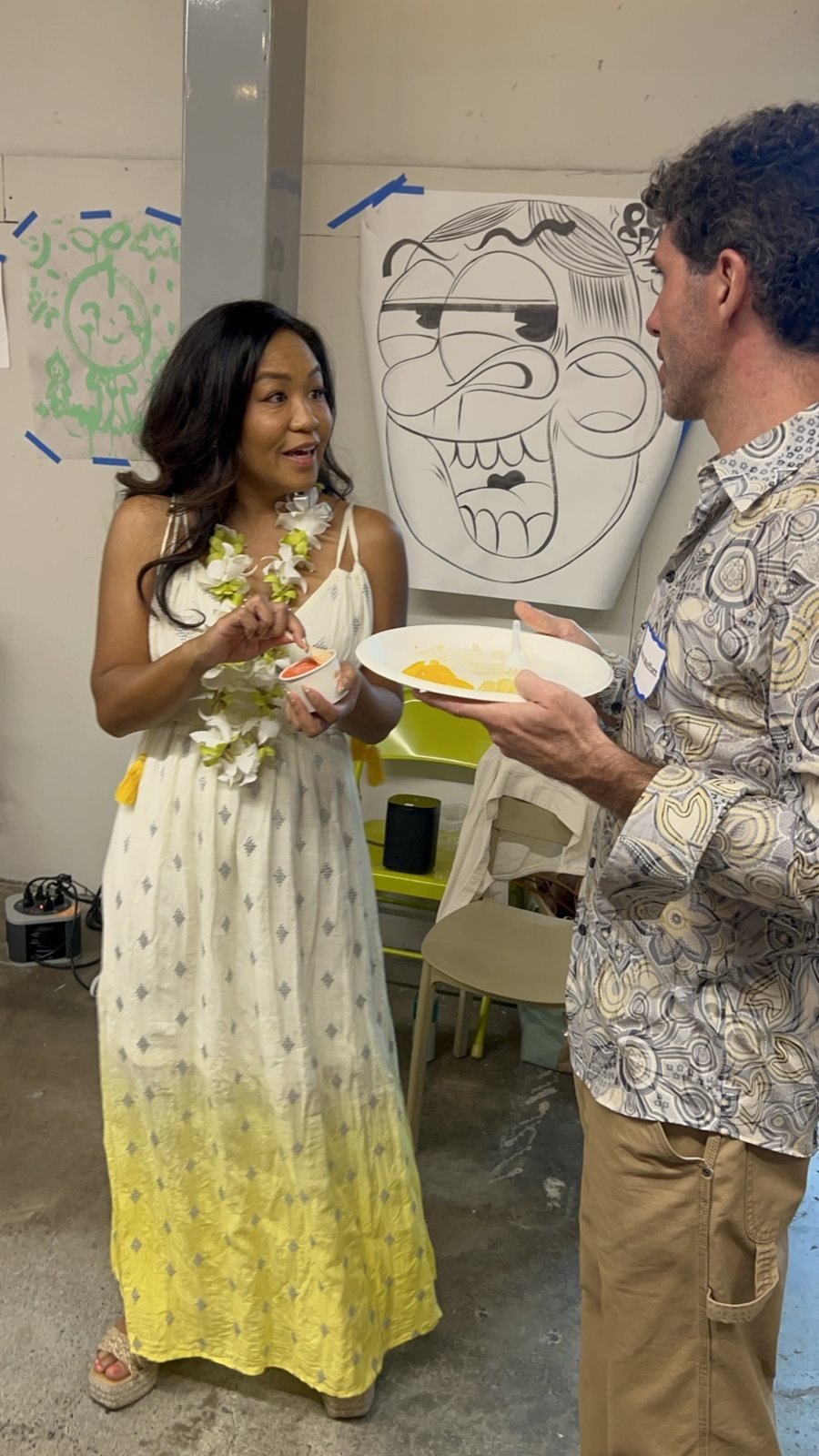 A woman in a long dress and a man talking beside a drawn poster