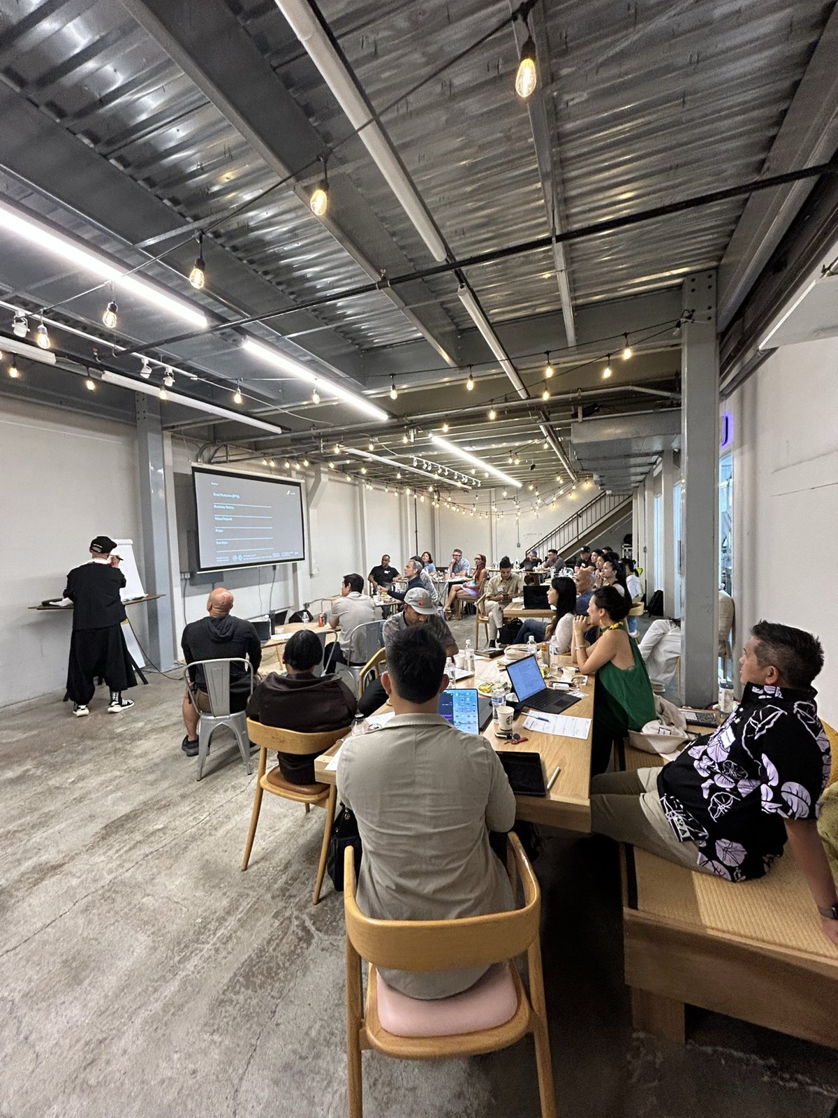 A long view of the workshop floor, attendees facing the screen