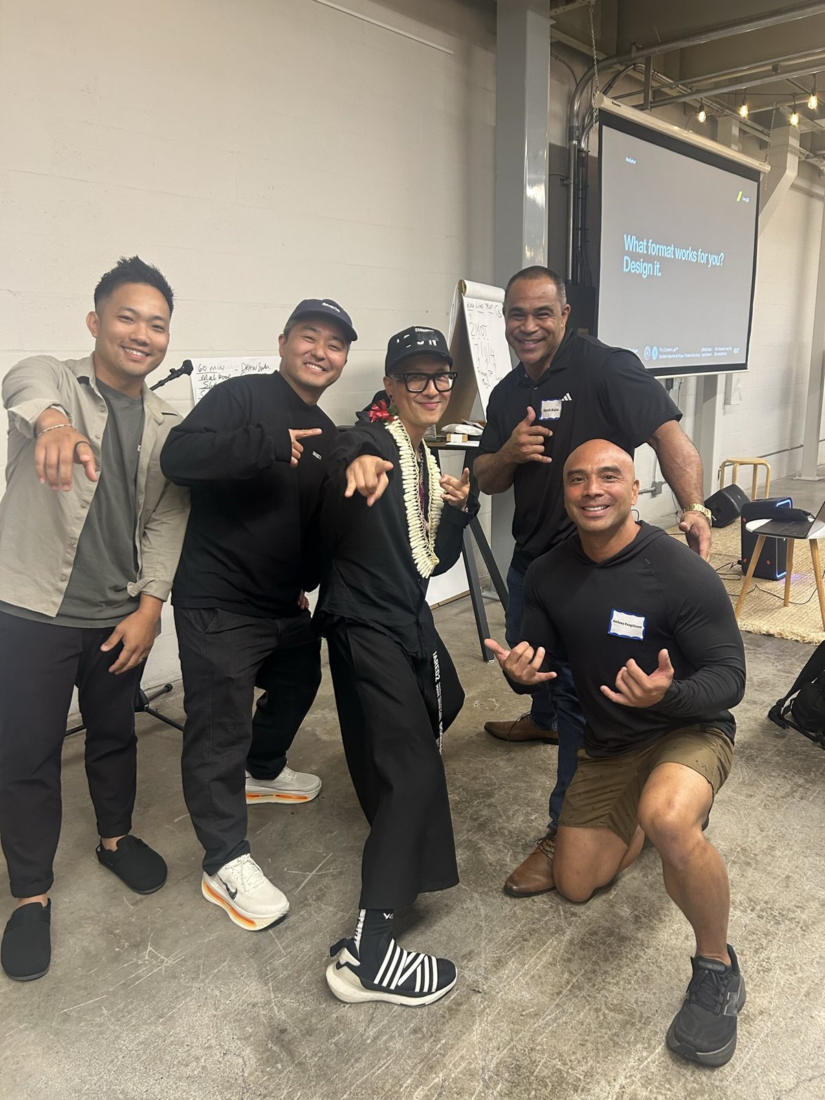 Five men posing and pointing at the camera in front of the screen